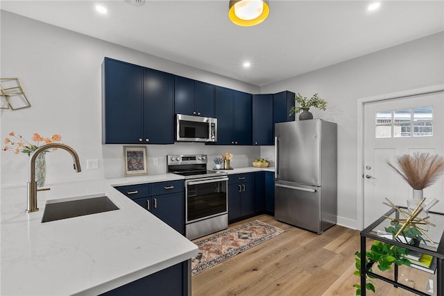kitchen with light wood finished floors, blue cabinetry, stainless steel appliances, and a sink