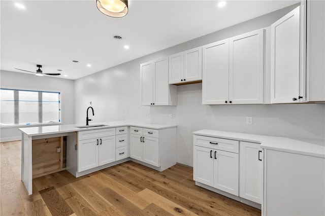 kitchen featuring light wood finished floors, a peninsula, white cabinets, and a sink