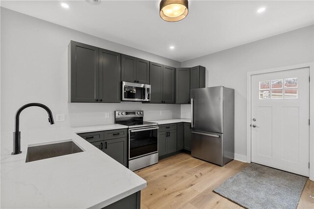 kitchen featuring recessed lighting, stainless steel appliances, light wood finished floors, and a sink