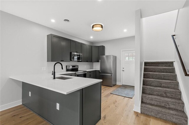 kitchen featuring a peninsula, appliances with stainless steel finishes, baseboards, and a sink