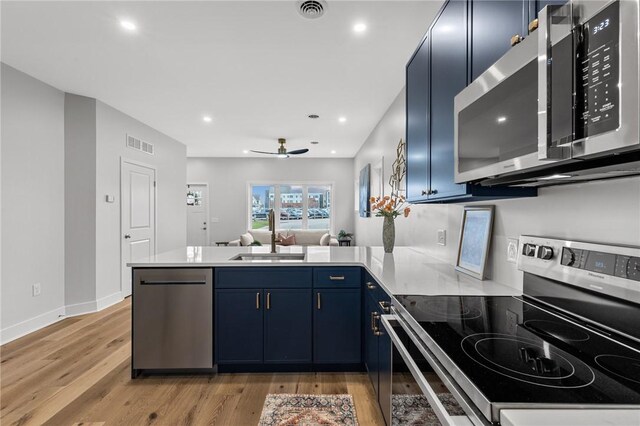 kitchen with stainless steel appliances, a peninsula, a sink, visible vents, and blue cabinetry