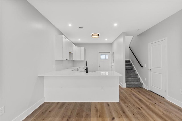 kitchen with white cabinets, a peninsula, a sink, light wood-type flooring, and light countertops