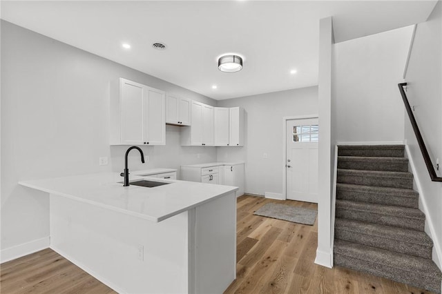 kitchen with a peninsula, baseboards, white cabinetry, and a sink