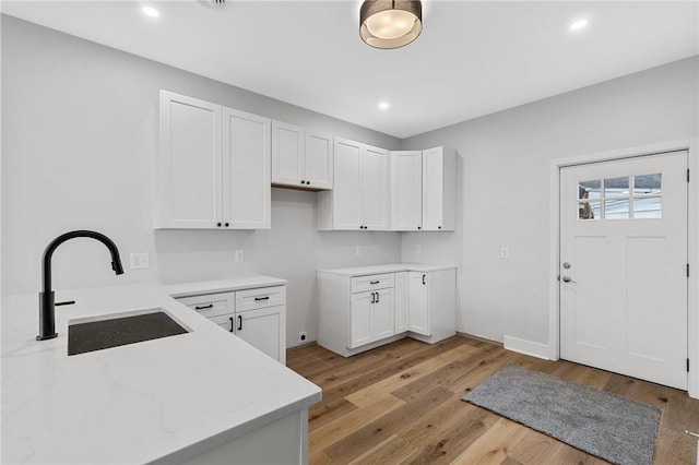 kitchen with a sink, light wood-style floors, white cabinetry, light stone countertops, and recessed lighting