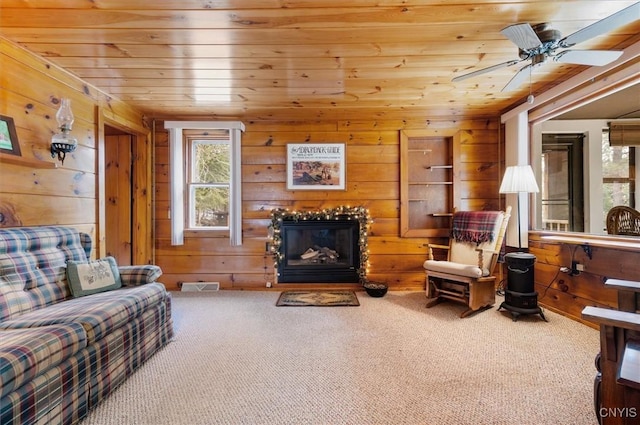 living area with a glass covered fireplace, visible vents, carpet, wood walls, and wood ceiling