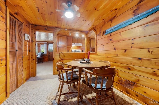 dining space with wooden walls, wooden ceiling, light colored carpet, and a ceiling fan