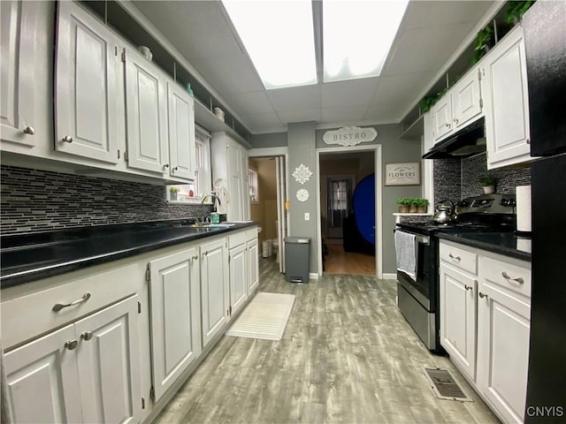 kitchen featuring electric stove, light wood-style flooring, white cabinets, backsplash, and under cabinet range hood