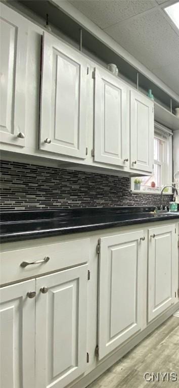 kitchen featuring white cabinets, a sink, light wood-type flooring, dark countertops, and backsplash