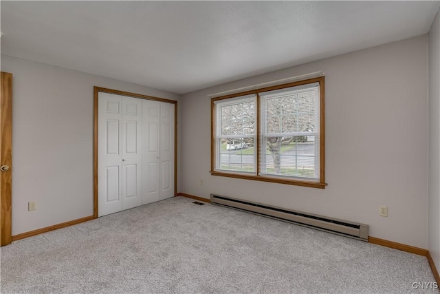 unfurnished bedroom featuring a baseboard heating unit, baseboards, carpet, and a closet