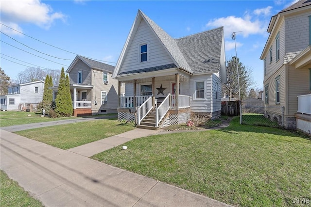 bungalow with a porch, a front lawn, fence, and roof with shingles
