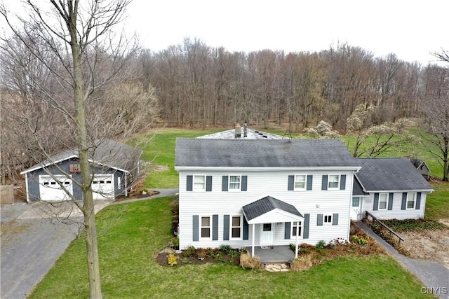 view of front of property featuring a detached garage, an outbuilding, a front lawn, and a view of trees