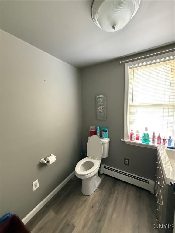 bathroom with baseboards, wood finished floors, a baseboard radiator, and toilet