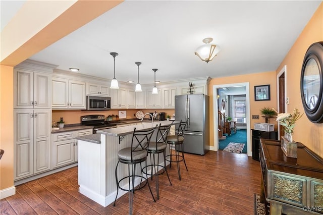 kitchen with stainless steel appliances, dark wood finished floors, dark countertops, pendant lighting, and a breakfast bar area