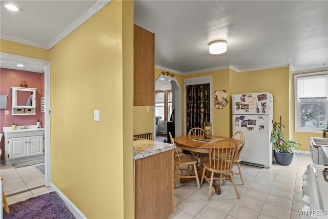 kitchen featuring light countertops, ornamental molding, light tile patterned floors, arched walkways, and freestanding refrigerator