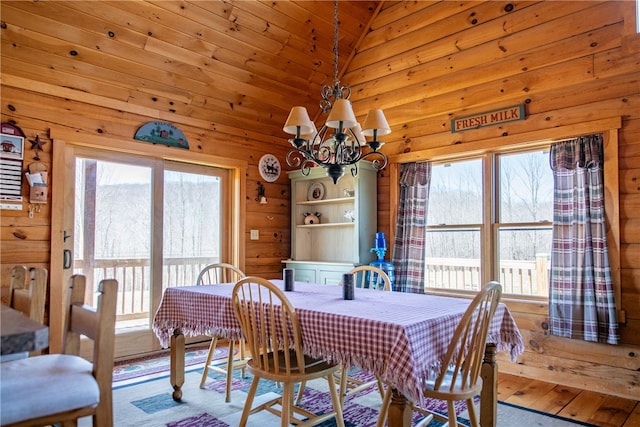 dining area featuring a chandelier, wooden walls, vaulted ceiling, and a wealth of natural light