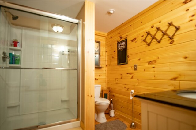 bathroom featuring a shower stall, toilet, vanity, and wooden walls
