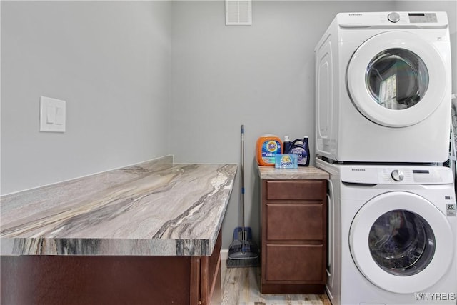 laundry room with cabinet space, light wood-style floors, stacked washer and dryer, and visible vents