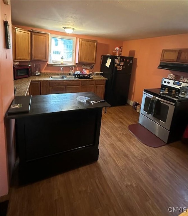 kitchen featuring wood finished floors, a sink, brown cabinetry, stainless steel appliances, and a peninsula
