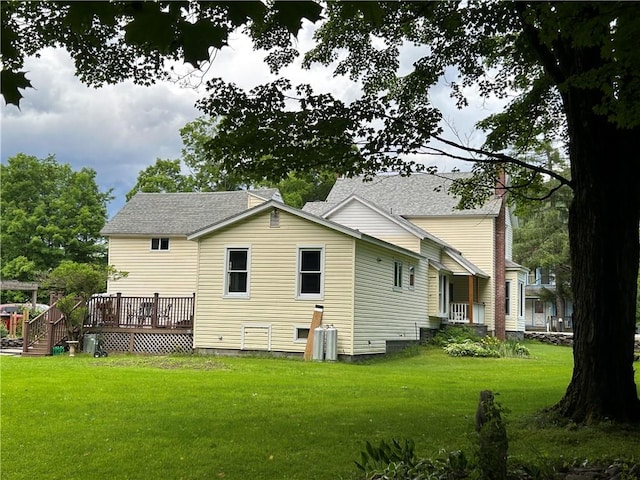 rear view of house with a yard, roof with shingles, and a deck