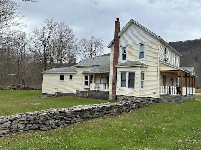 back of property with a lawn, a chimney, and covered porch
