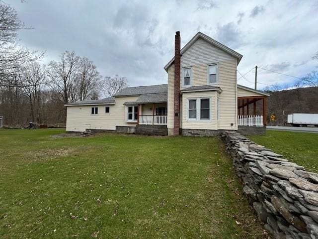 back of house with a chimney, a yard, and covered porch