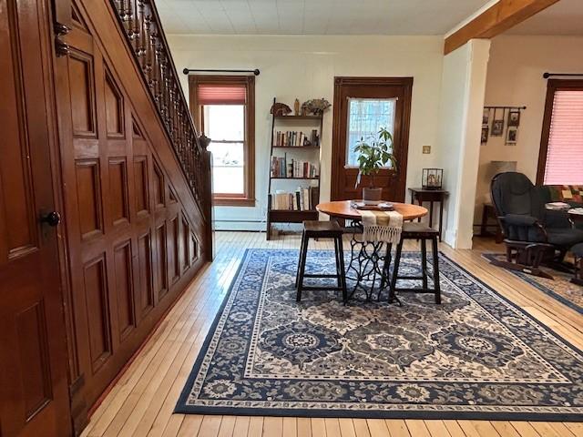 dining room with a baseboard heating unit, a healthy amount of sunlight, stairs, and light wood-style flooring