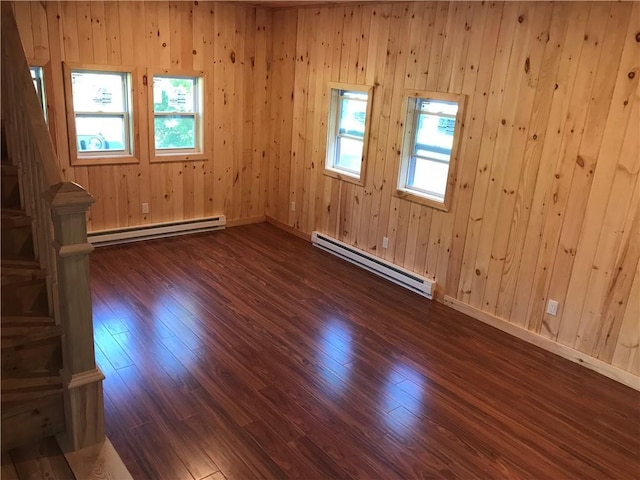 empty room featuring a baseboard heating unit, baseboards, stairs, and dark wood-style floors