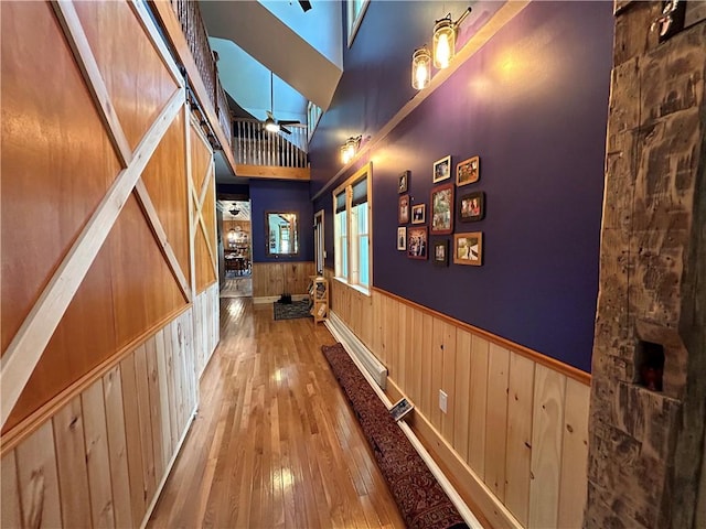 corridor with hardwood / wood-style flooring, wood walls, a high ceiling, and a wainscoted wall