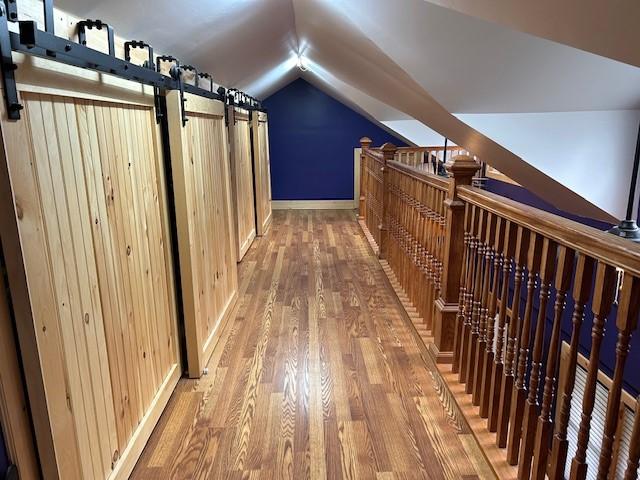 corridor featuring lofted ceiling, wood finished floors, and baseboards