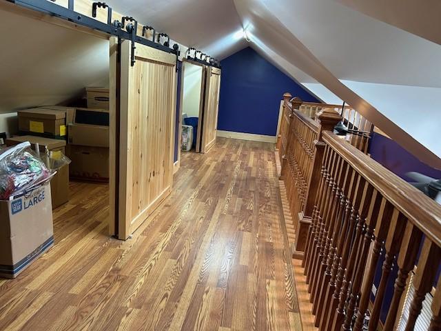 additional living space with a barn door, vaulted ceiling, baseboards, and light wood-type flooring