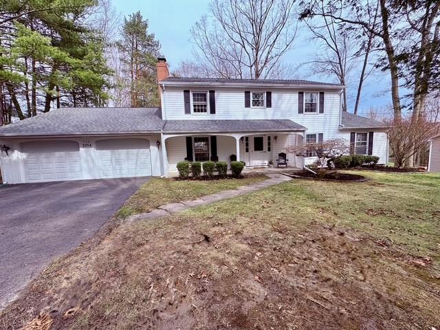 traditional-style house featuring a garage, a chimney, aphalt driveway, a porch, and a front yard