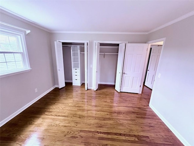 unfurnished bedroom with two closets, baseboards, crown molding, and wood finished floors