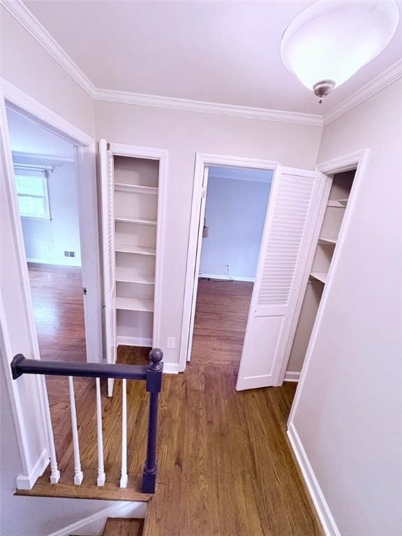 hall featuring built in shelves, crown molding, baseboards, and dark wood-style flooring