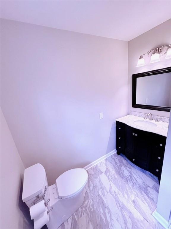 half bath with baseboards, marble finish floor, vanity, and toilet