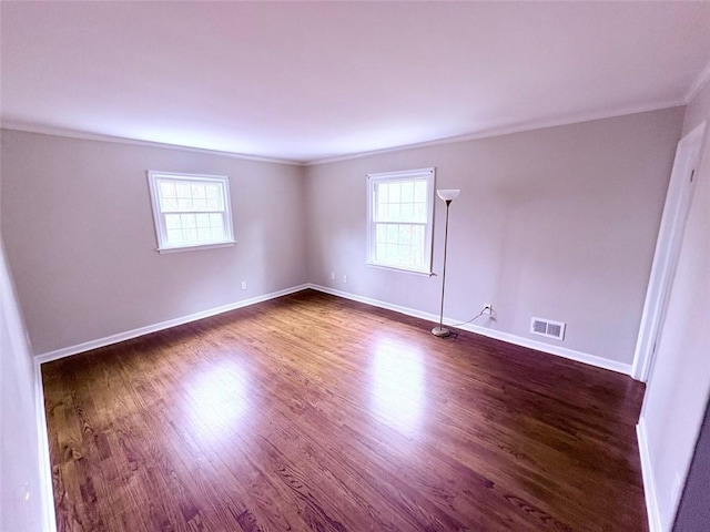 empty room featuring visible vents, a wealth of natural light, dark wood-type flooring, and crown molding