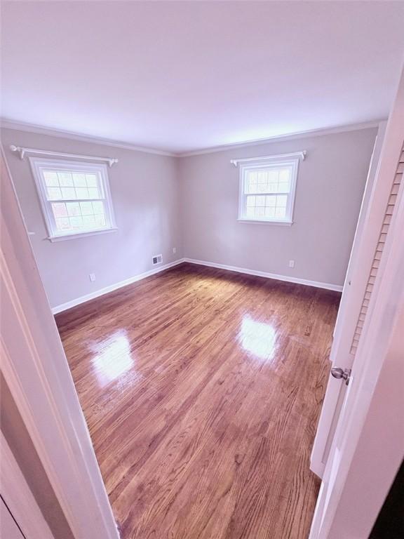 unfurnished bedroom featuring visible vents, wood finished floors, and ornamental molding