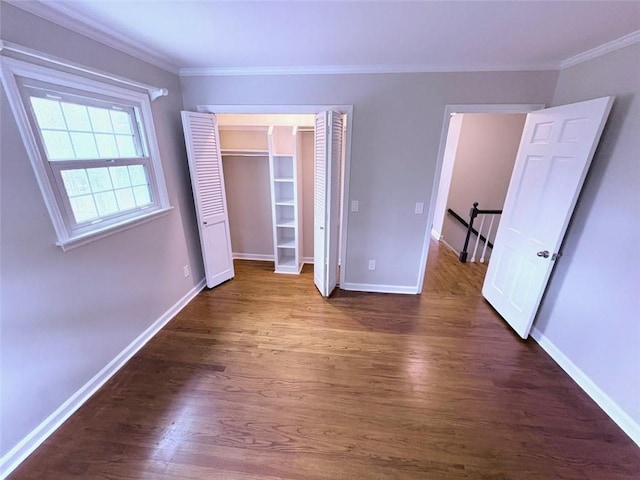 unfurnished bedroom with baseboards, crown molding, dark wood-style floors, and a closet