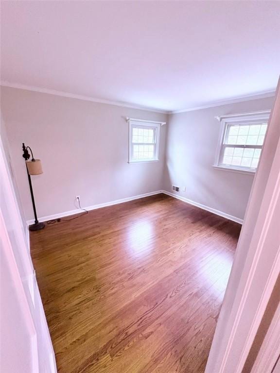 empty room with dark wood-style flooring, ornamental molding, visible vents, and baseboards