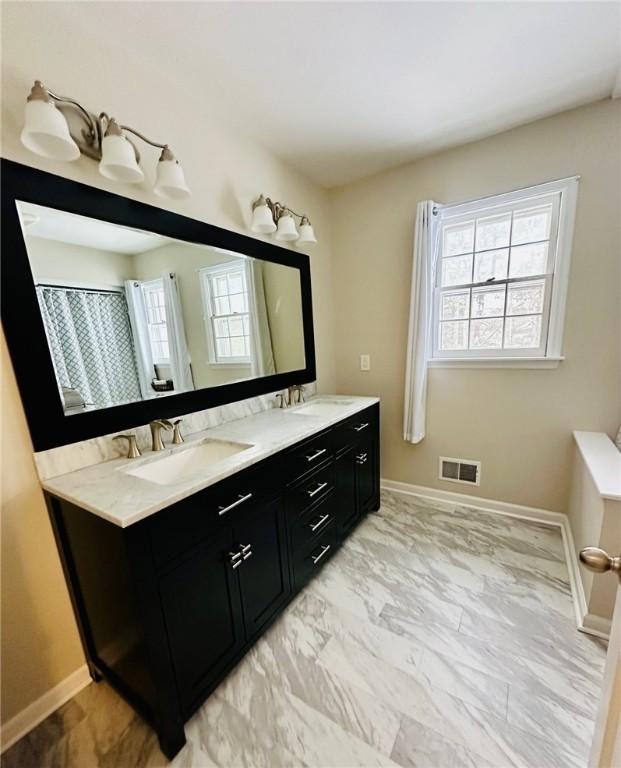 full bath with a sink, double vanity, baseboards, visible vents, and marble finish floor