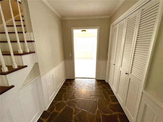 hallway with a wainscoted wall, stone floors, stairway, a decorative wall, and ornamental molding