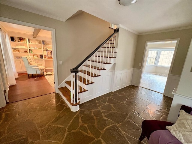 staircase featuring a decorative wall, wainscoting, built in features, stone flooring, and ornamental molding