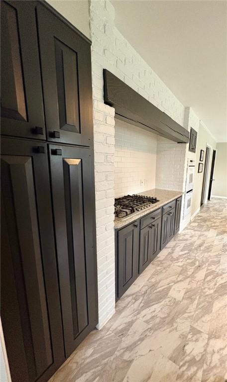 kitchen featuring oven, exhaust hood, baseboards, decorative backsplash, and stainless steel gas cooktop