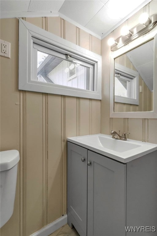 bathroom featuring lofted ceiling, a decorative wall, toilet, and vanity