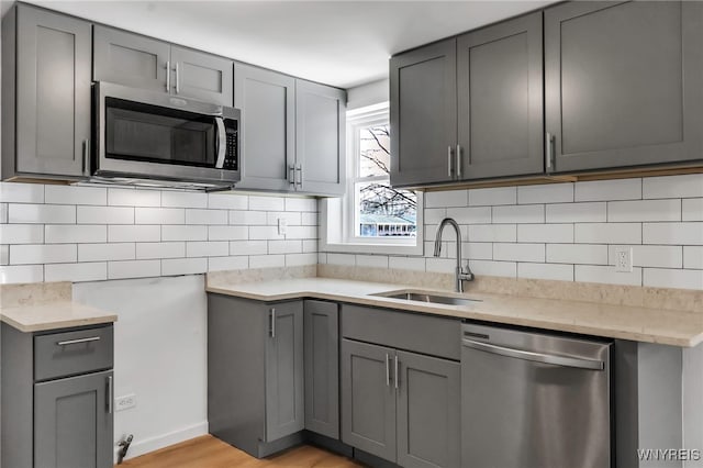 kitchen featuring stainless steel appliances, gray cabinetry, a sink, and backsplash