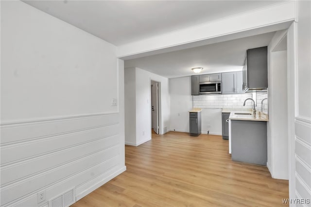 kitchen with tasteful backsplash, light wood-style floors, gray cabinets, light countertops, and stainless steel microwave