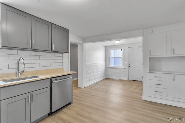 kitchen with stainless steel dishwasher, light countertops, a sink, and gray cabinets