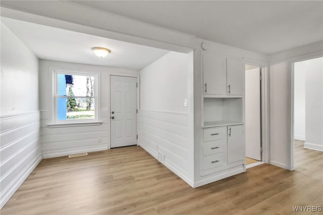 foyer entrance with baseboards, a wainscoted wall, light wood-style floors, and visible vents