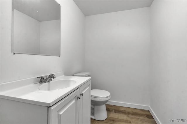 half bathroom with toilet, vanity, wood finished floors, and baseboards