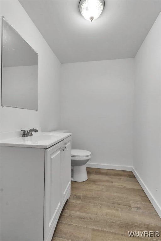 half bath with baseboards, wood finished floors, vanity, and toilet