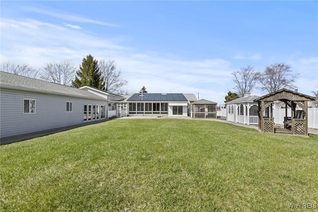 rear view of house with a sunroom, a lawn, a gazebo, and solar panels